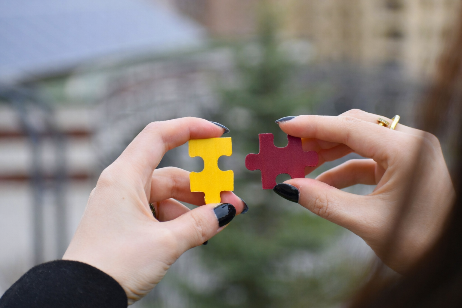 Hands holding yellow and maroon puzzle pieces, representing the hidden truths of grief, the pieces we carry alone, and the slow process of finding what fits.